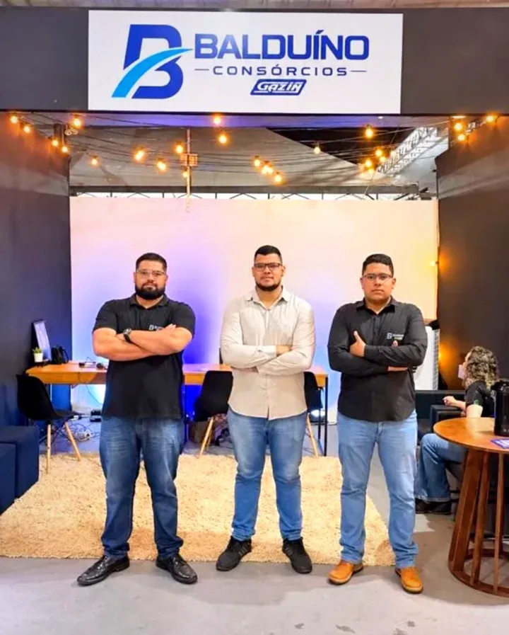Equipe da Balduíno Consórcios no estande, abaixo da placa com o logo Balduíno e o selo Gazin
